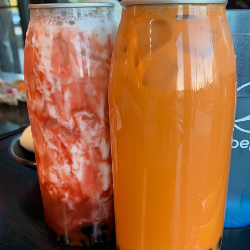 Two tall drinks, one strawberry-swirled and one orange, on a dark surface.