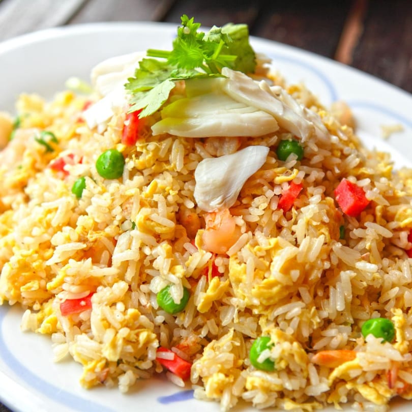 Crab fried rice with peas, red peppers, shrimp, and cilantro on a white plate.