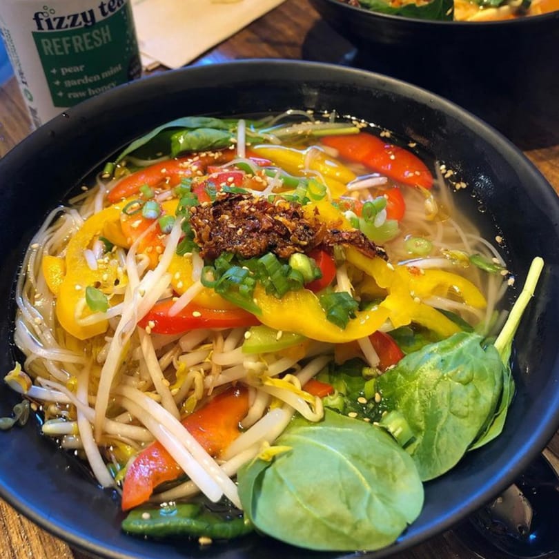 A close-up of a vibrant noodle bowl with bell peppers, bean sprouts, spinach, and chili flakes.