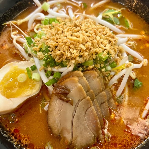 Close-up of a spicy ramen bowl with pork, egg, bean sprouts, green onions, and crispy garlic.